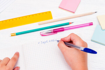 Children's hands close up writing on September 1 in a notebook. Pens, pencils, ruler, colored stickers on the table. Back to school concept.Copy space for text.
