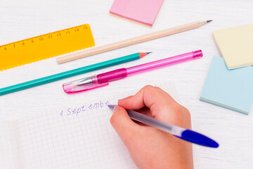 Children's hands close up writing on September 1 in a notebook. Pens, pencils, ruler, colored stickers on the table. Back to school concept.Copy space for text.
