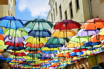 colorful umbrellas hanging between buildings over blue sky - obrazy, fototapety, plakaty