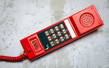 Old, retro red push-button telephone on the background of a plastered wall.
