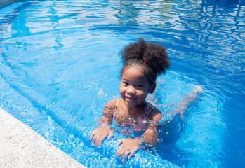 Portrait of Cute little girl African-American in swimming suit sitting in a water pool on a summer day.