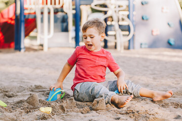 Caucasian child sitting in sandbox playing with beach toys. Baby building sandcastle sand pie....