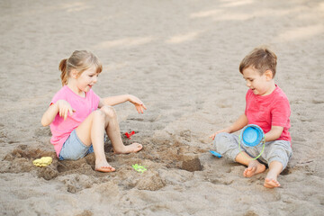 Two Caucasian children sitting in sandbox playing with beach toys. Little girl and boy friends having fun together on playground. Summer outdoors activity for kids. Leisure time lifestyle childhood.