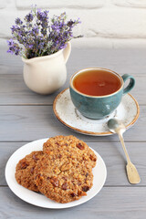 Oatmeal cookies with walnuts and raisins on a saucer and a cup of herbal tea on a gray wooden table. Closeup