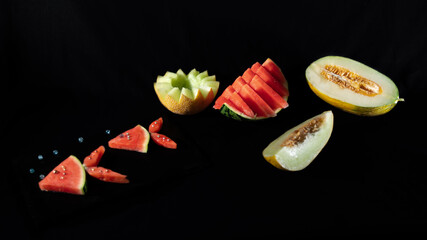 Summer fruits on a black background, nicely cut melons and fish-shaped watermelons