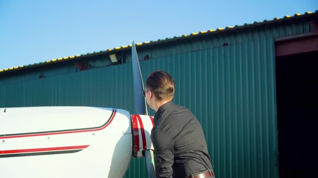 Side view of a male pilot twists an airplane propeller