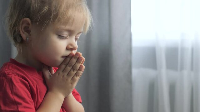 little daughter girl makes a wish prayers lifestyle bedtime religion concept . prayer child indoors praying by bed in front of window