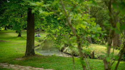 
Nice view between the trees of the lake that winds through the vegetation, in the distance a couple sitting in the grass