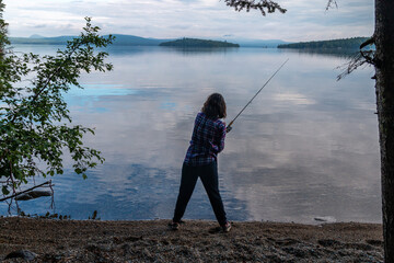 A woman fishing on an island in Maine. - 363389664