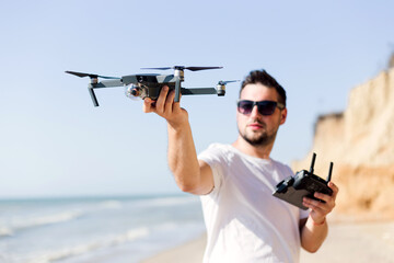 Young man holding drone before flight near ocean or sea. Pretty guy prepare to pilot outdoor - Powered by Adobe