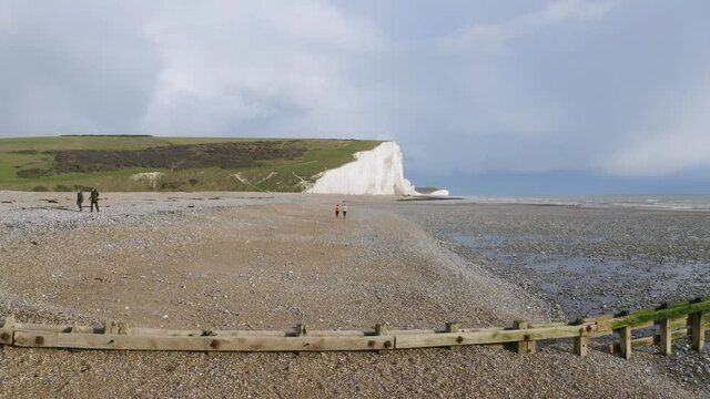 Aerial drone shot flying low and fast towards and over runners on beach running with Seven Sisters cliffs in the background