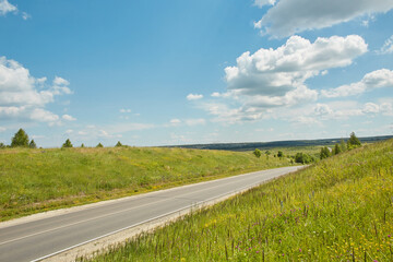 Highway road up hill through green grass field under white clouds on blue sky in summer day. Natural Landscape of Road and Landscape Scenery. Road trip travel concept.