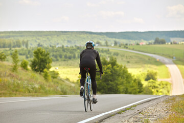 A professional cyclist rides on an empty highway going down a hill, beautiful nature on the horizon on a Sunny day.