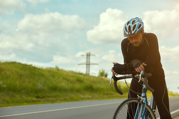 Portrait of a professional cyclist in sportswear wearing a helmet standing with a Bicycle on an open road wearing sunglasses against the sky