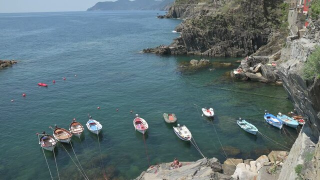 Riomaggiore, Liguria, Italy. June 2020. Tilt footage on the marina: moored boats swing on crystal clear water, behind the Cinque Terre coastline