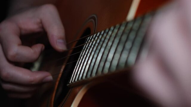 Man playing classic, acoustic guitar and performing bard songs. Concept. Close up of male hands playing guitar, taking chords in the dark room, live music.