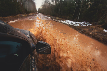 Suv offroad 4wd car rides through muddy puddle, off-road track road, with a big splash, during a...