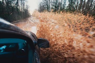 Suv offroad 4wd car rides through muddy puddle, off-road track road, with a big splash, during a...