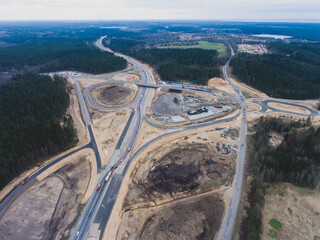 Aerial air view of a massive construction site with a heavy vehicle, bulldozer and excavator, building a new road, working and unloading sand and road metal during construction, shot from drone