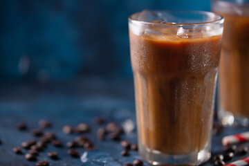 Cold coffee with ice cubes and milk on a background with coffee grains and tubes, dark blue background, summer, cool drinks