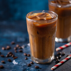 Cold coffee with ice cubes and milk on a background with coffee grains and tubes, dark blue background, summer, cool drinks