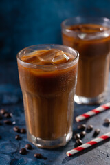 Iced coffee in a glass with cream, or milk and coffee beans. Cold summer drink on a blue background