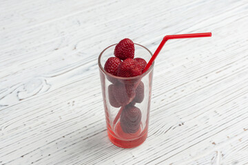 transparent glass with strawberries and red tuba on a wooden white table