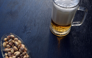 
a glass of fresh beer and pistachios are on the table