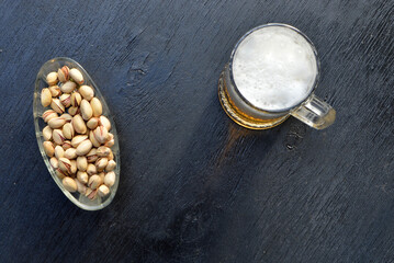 
mug of beer and pistachios stand on black wooden background