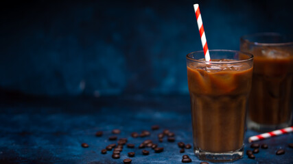 Cold coffee with ice cubes and milk on a background with coffee grains and tubes, dark blue background, summer, cool drinks