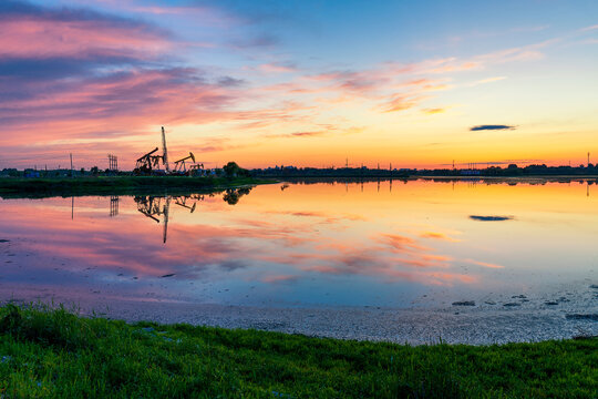 Oil Pumping Unit by the lake in the sunset.