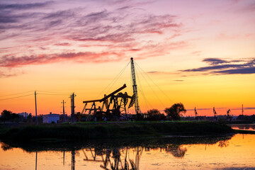 Oil Pumping Unit by the lake in the sunset.