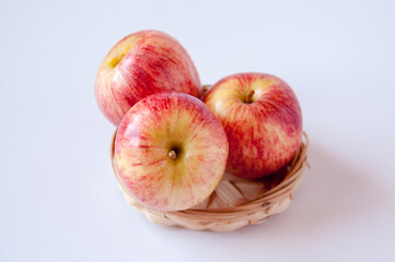 Three red apples in a wicker plate on a white background