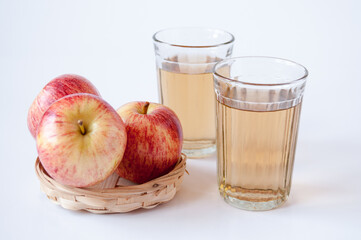 Three red apples in a wicker plate and two glasses of Apple juice on a white background