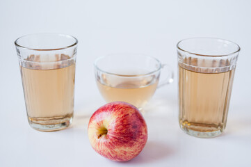 A mug and glass of Apple juice and a red Apple on a white background