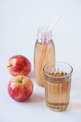 A bottle with straws and a glass of Apple juice and two red apples on a white background