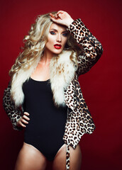 Beautiful fashionable girl with blond hair wearing a leopard print jacket posing on a red...