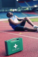 First aid kid, male athlete clasping leg in pain in the background