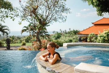 Young caucasian woman relaxing at spa pool, hold flower in hr hands.  Beautiful woman relaxing in outdoor spa swimming pool. Closeup face of attractive girl enjoy vacation at resort.