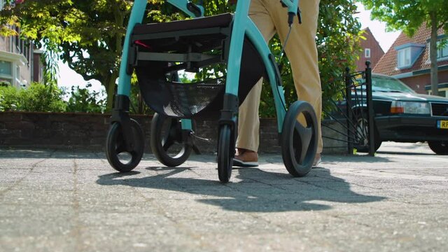 Low angle shot of senior citizen using walking aid in sunny suburban, slowmo