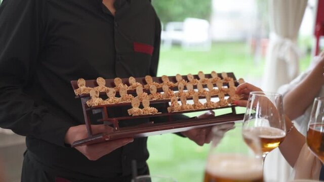 Server in black uniform offering deserts to guests of an outdoor event