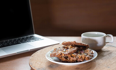 Cookie made by Grain , Raisin ,Almond, Pumpkin Seed, Cashew Nut, Cranberry , Walnut, Sunflower Seed, Chia Seed,Black Sesame Seed with a background of laptop and a cup of black coffee on wooden table