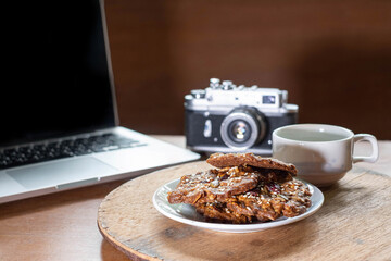 Cookie made by Grain , Raisin ,Almond, Pumpkin Seed, Cashew Nut, Cranberry , Walnut, Sunflower Seed, Chia Seed,Black Sesame Seed with a background of laptop and a cup of black coffee on wooden table