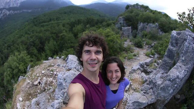 A woman and a man take a selfie on top of a mountain, a girl and her husband take pictures against the backdrop of a mountain valley, a trip to the picturesque places, a couple travels together