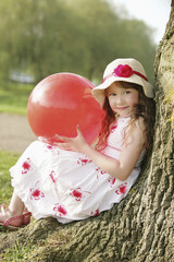 Girl with red ball, leaning against tree