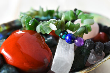 A close up image of a jade bracelet and a chakra bracelet in a bowl filled with healing crystals. 