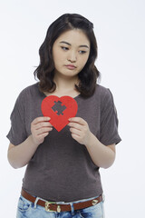 Sad woman holding up a red heart shape with a missing puzzle piece