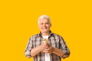 Senior man with cute duckling on color background