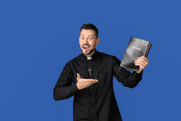 Handsome priest with Bible on color background
