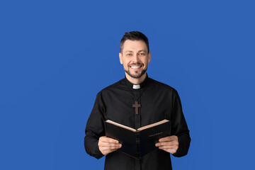 Handsome priest with Bible on color background - obrazy, fototapety, plakaty